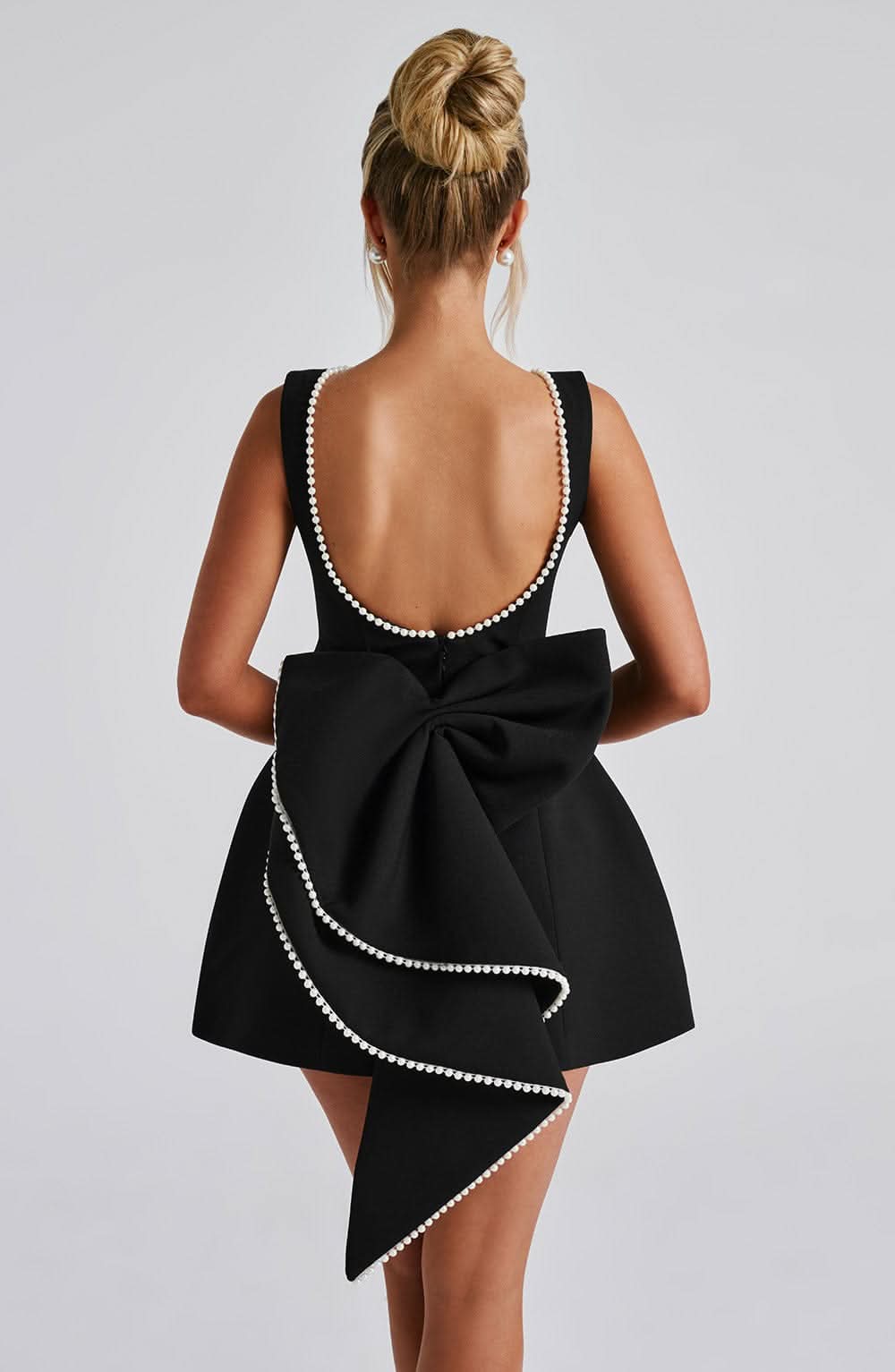 Black mini dress with pearl-trimmed backless design and oversized bow detail