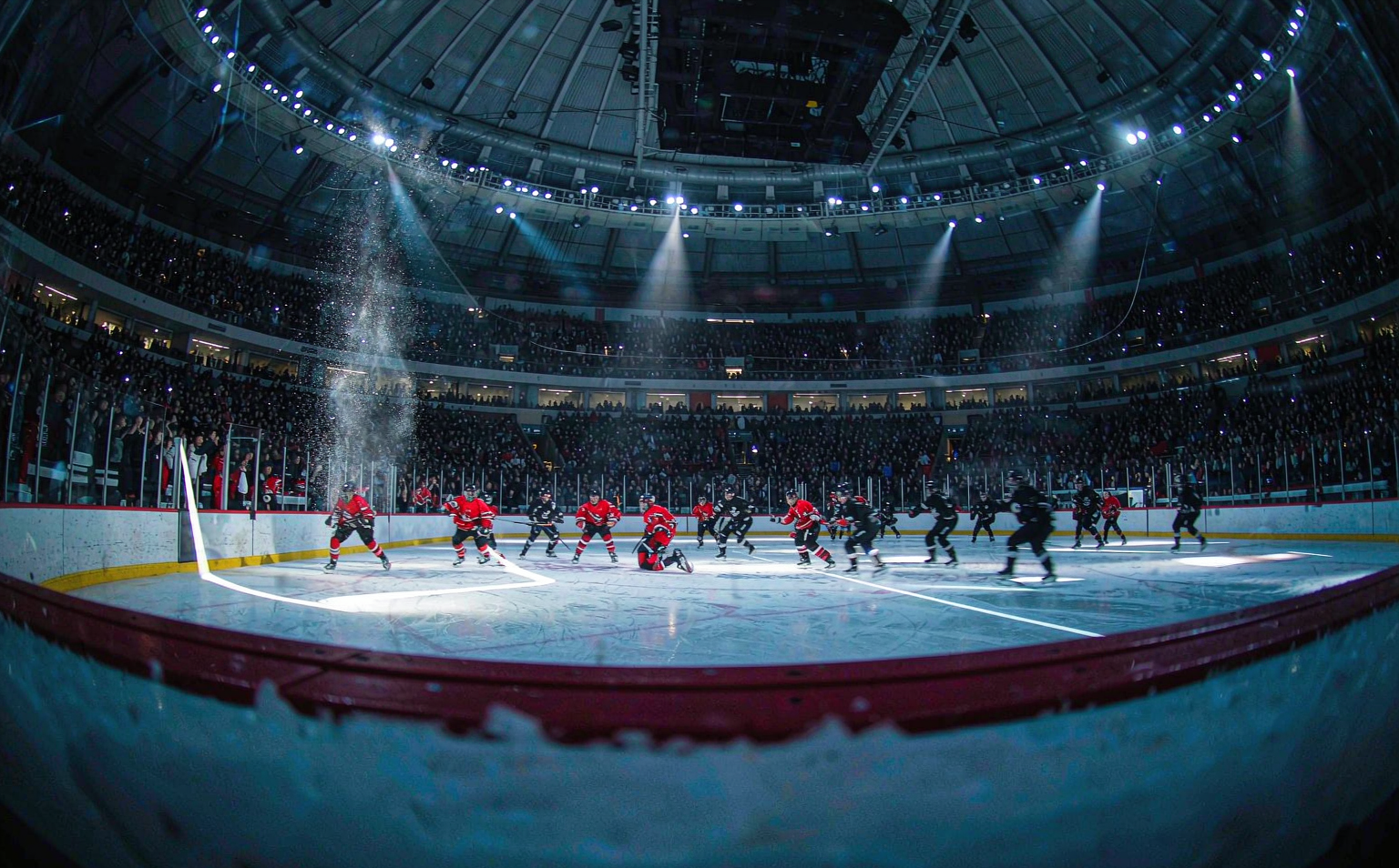 Ice hockey arena glowing under spotlights with packed crowd in plain team-color sweaters