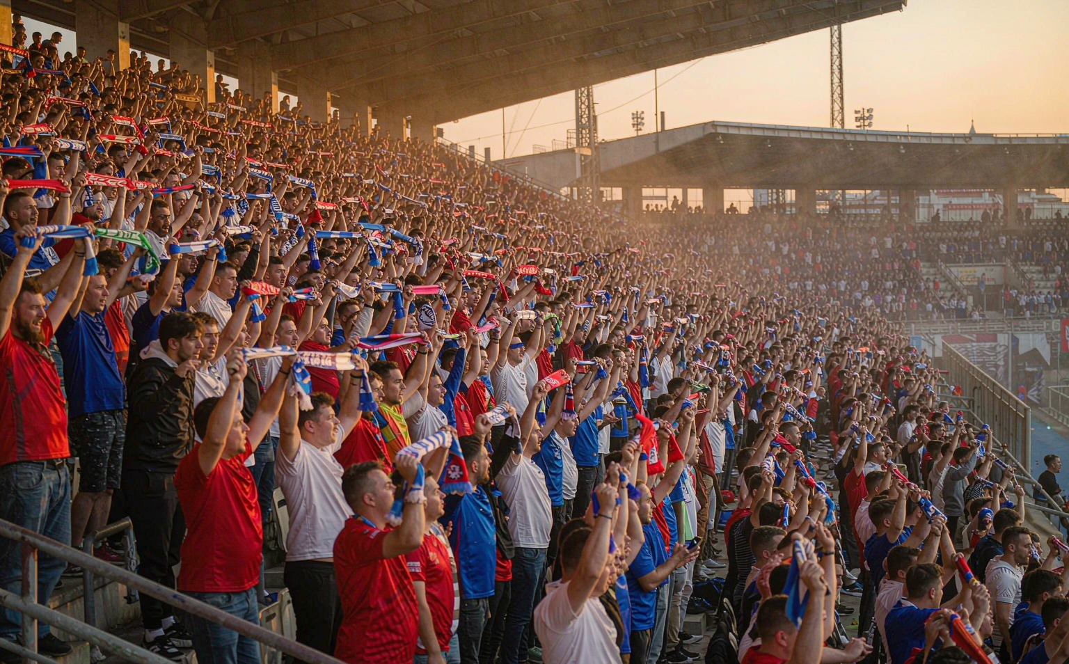 European football stadium terrace packed with supporters in plain club-color shirts