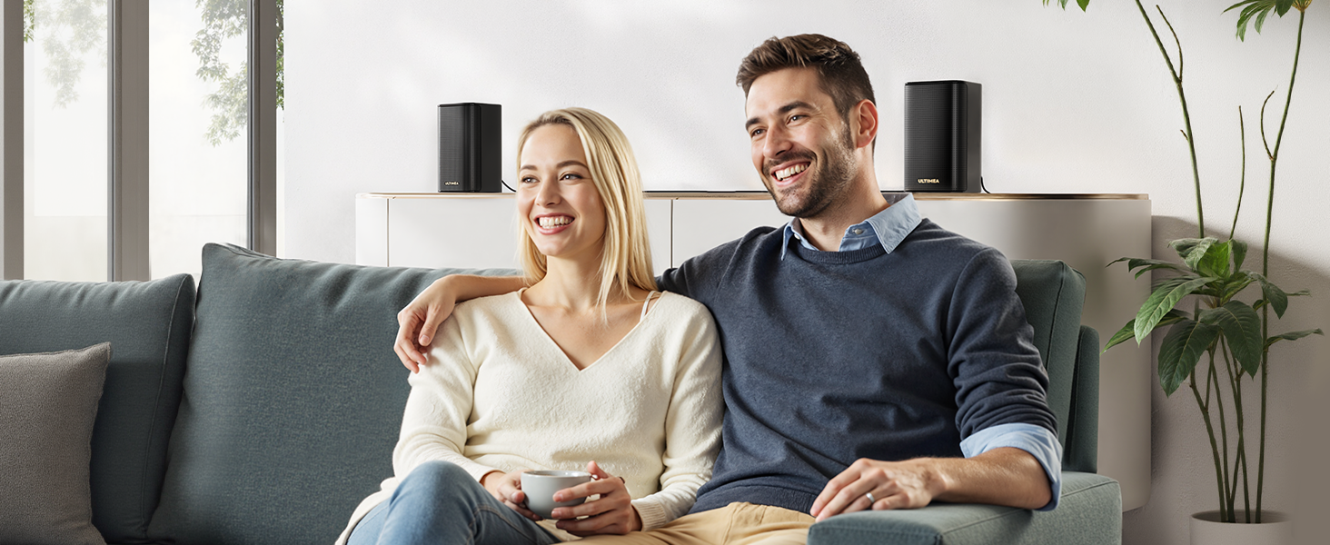 Escena interior que muestra a una pareja sentada en un sofá gris en una moderna sala de estar con una planta de interior en el fondo.