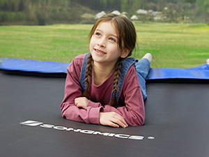 Trampolín grande para exteriores con superficie de salto negra. Persona acostada en un trampolín rodeada