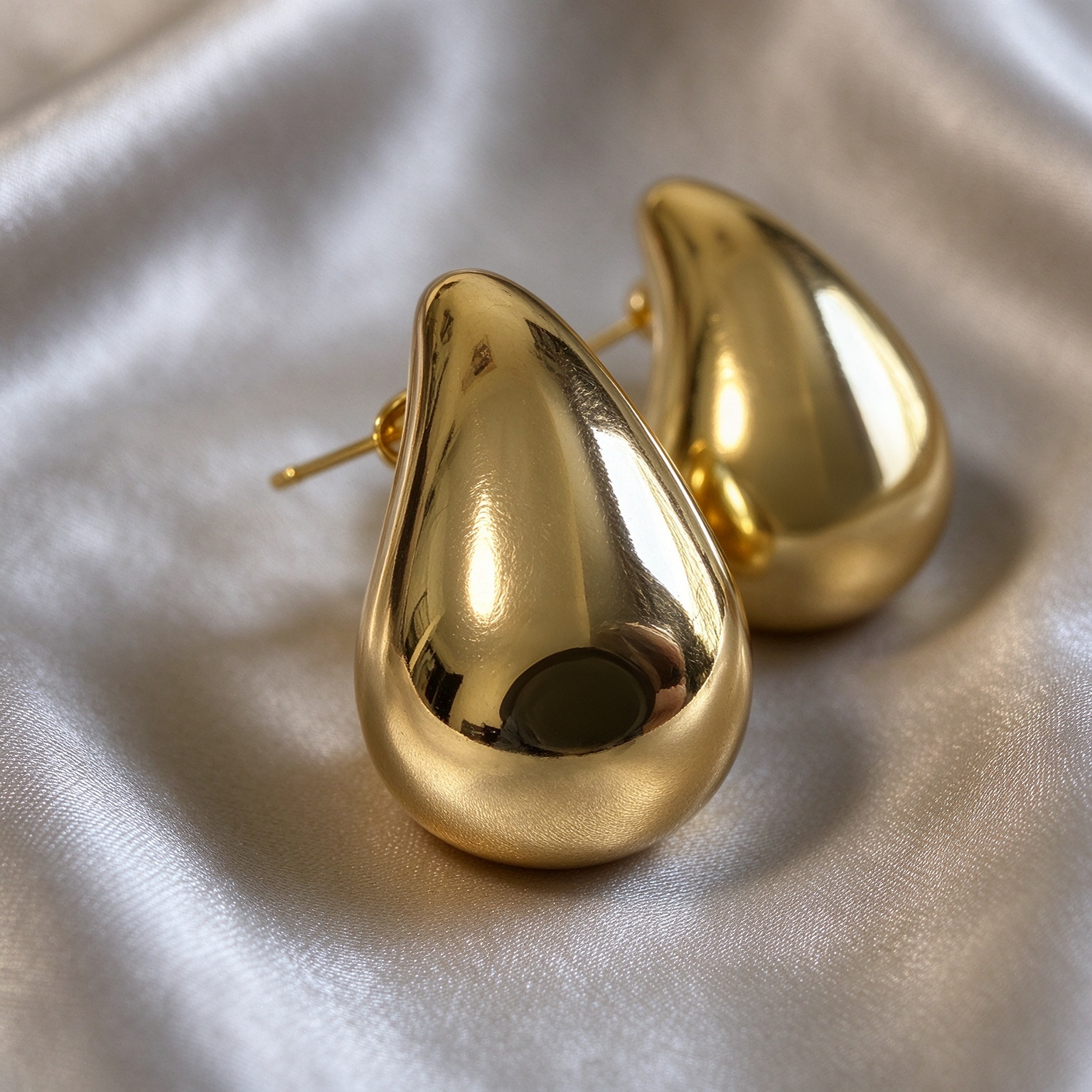 Close up detail of gold teardrop earrings, polished mirror finish, rounded drop shape, fine jewelry detail shot