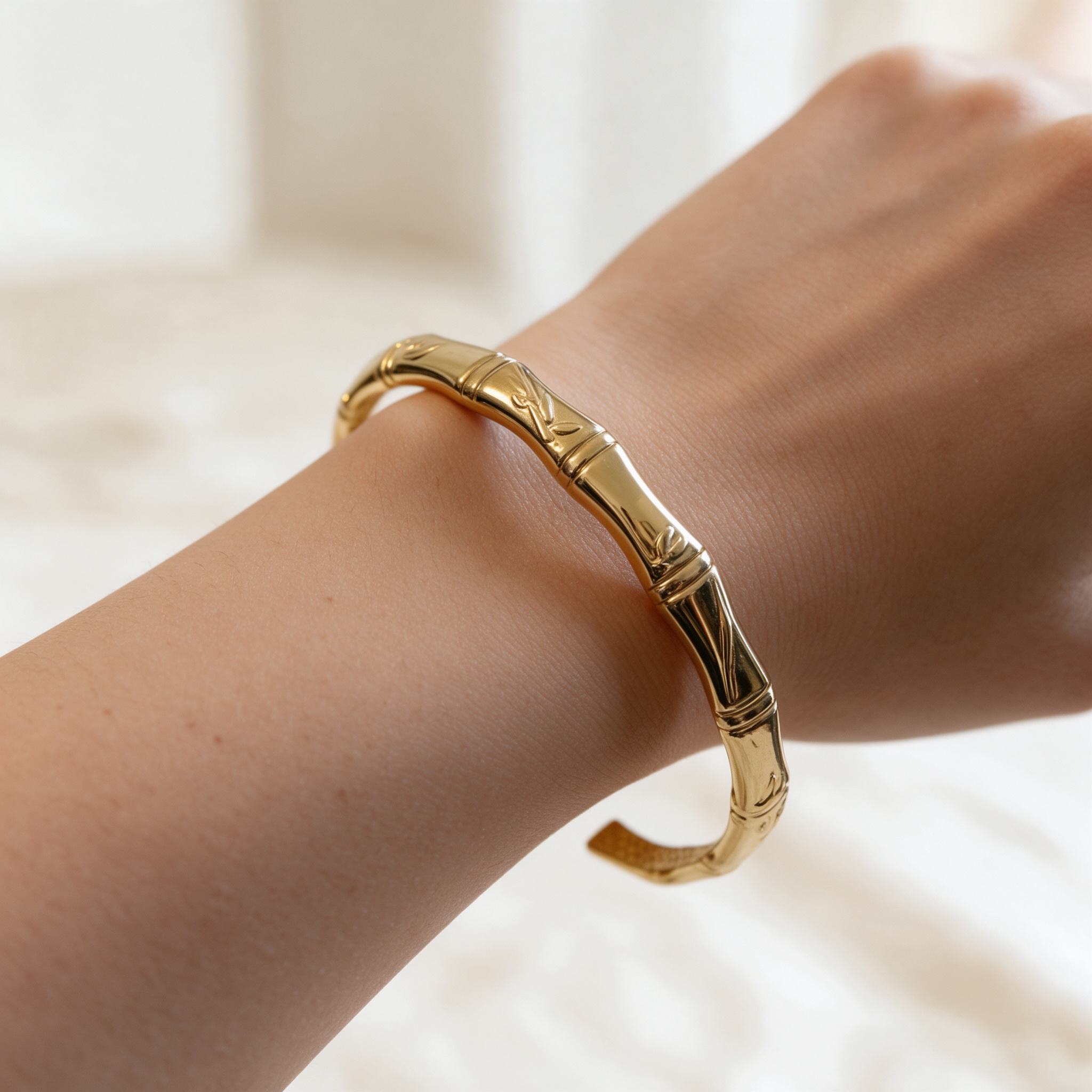 Natural skin tone model wearing gold bamboo open cuff bracelet, wrist closeup jewelry photo