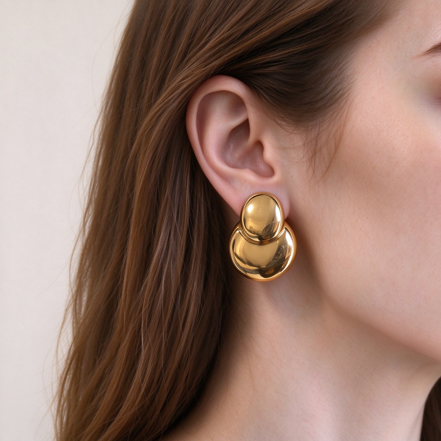Natural skin tone model wearing gold double bubble statement earrings, closeup jewelry photo