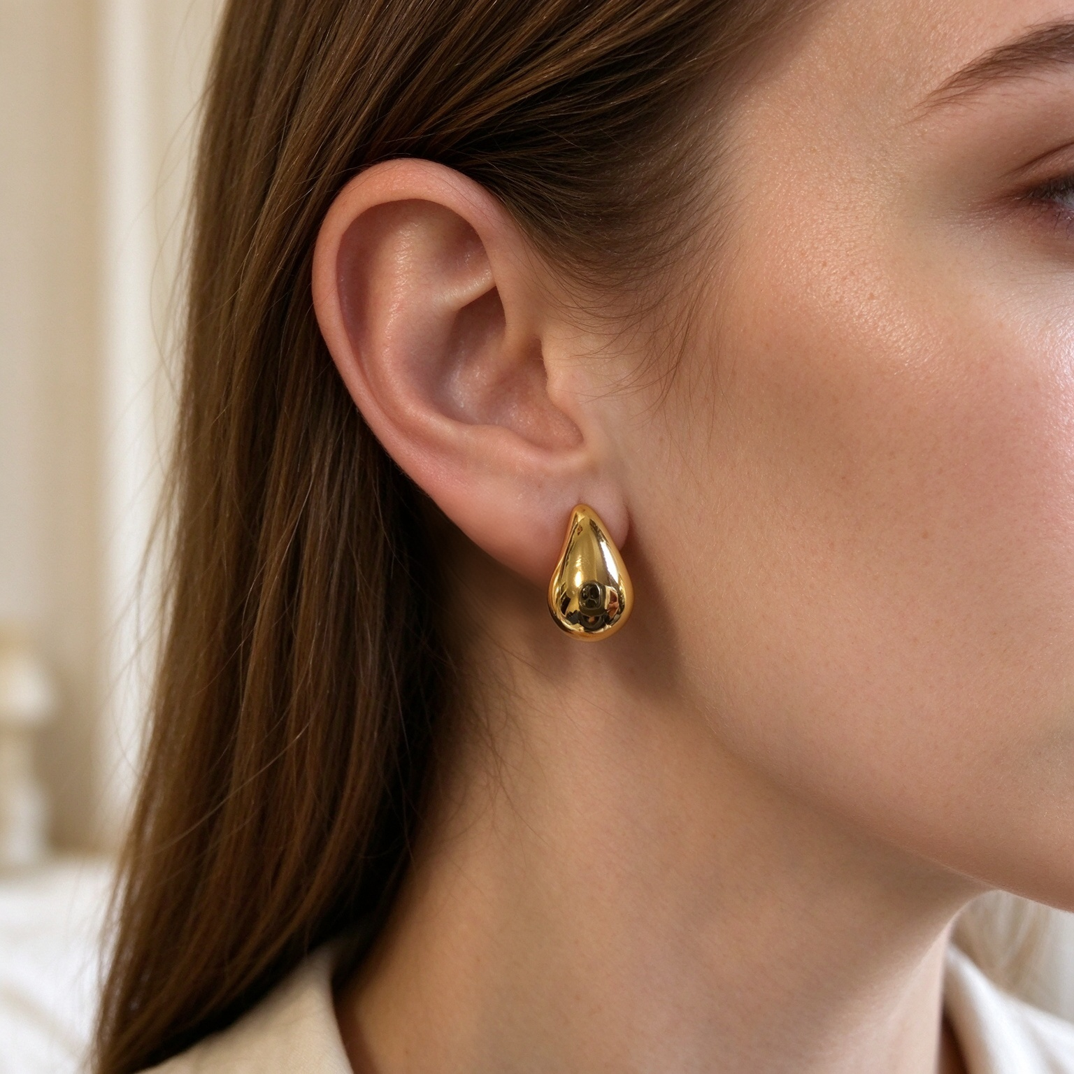 Natural skin tone model wearing gold teardrop statement earrings, closeup jewelry photo