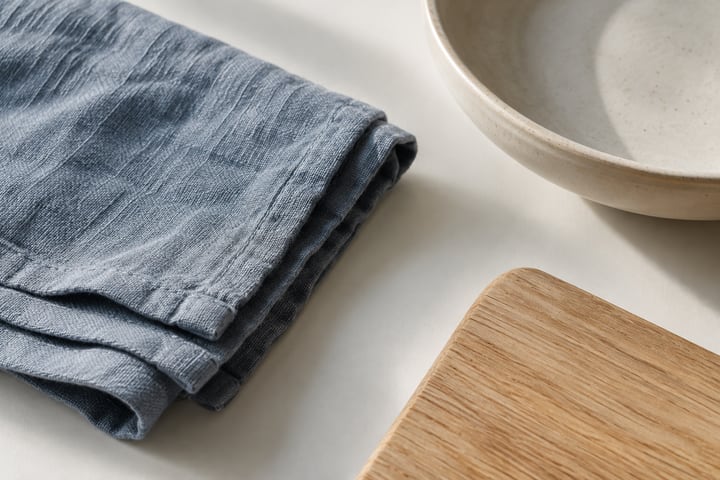 Blue-gray cotton fabric beside an ivory dish and oak board