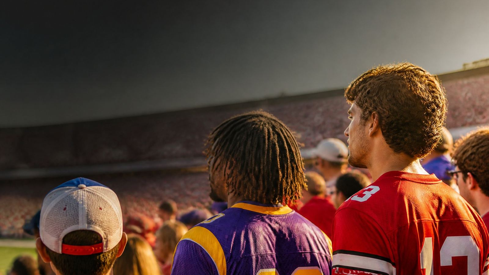 College football fans cheering in stadium stands wearing crimson, purple and gold jerseys