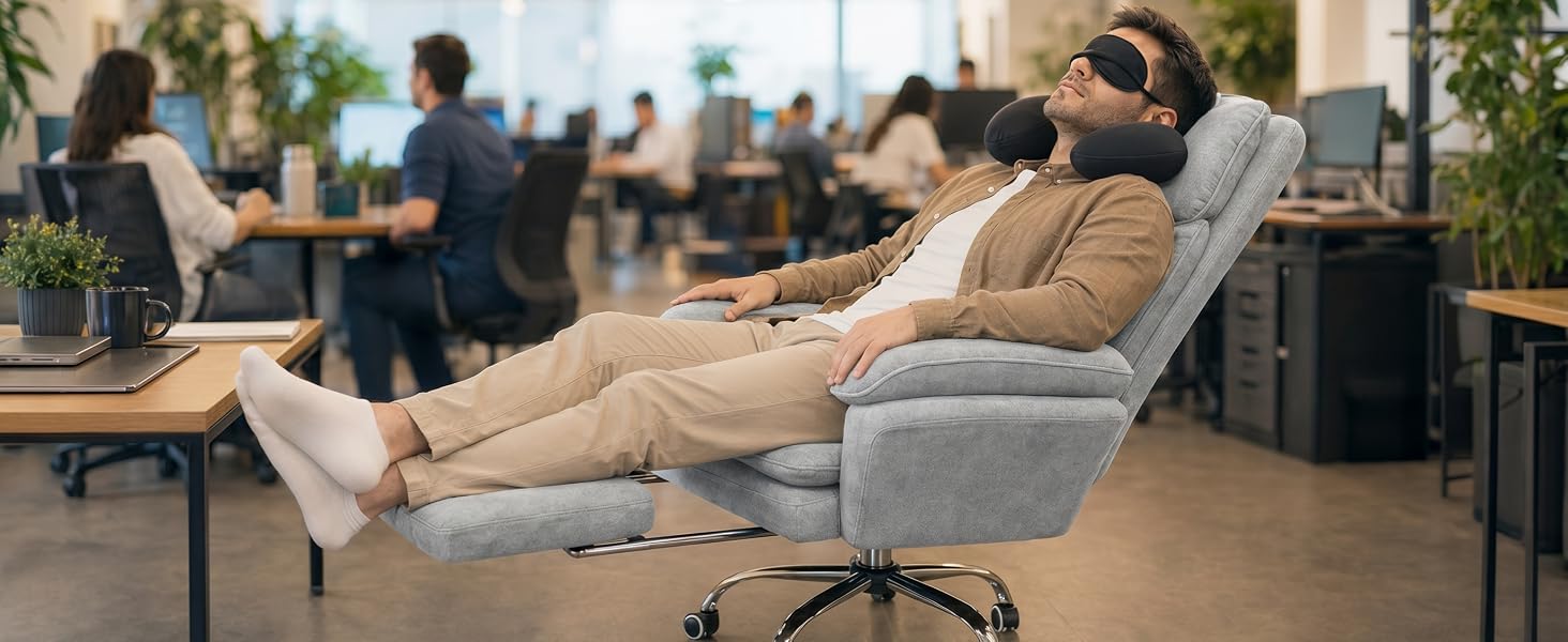 Silla de oficina tapizada gris con reposapiés extendido en un entorno de trabajo moderno. Varias personas y mesas de madera visible w tle biura rozmytego.