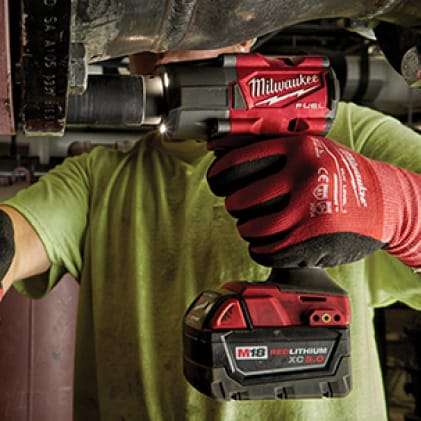 Milwaukee 2658-20-48-59-1850 M18 18V Lithium-Ion Cordless 3/8 in. Impact Wrench W/ Friction Ring W/ M18 Starter Kit (1) 5.0Ah Battery & Charger Man wearing work gloves uses an M18 FUEL 1/2" Mid-Torque Impact Wrench to remove a large bolt.