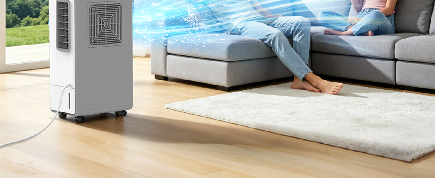 Portable air conditioning unit positioned on floor beside bed with person's legs visible on mattress in bright room.