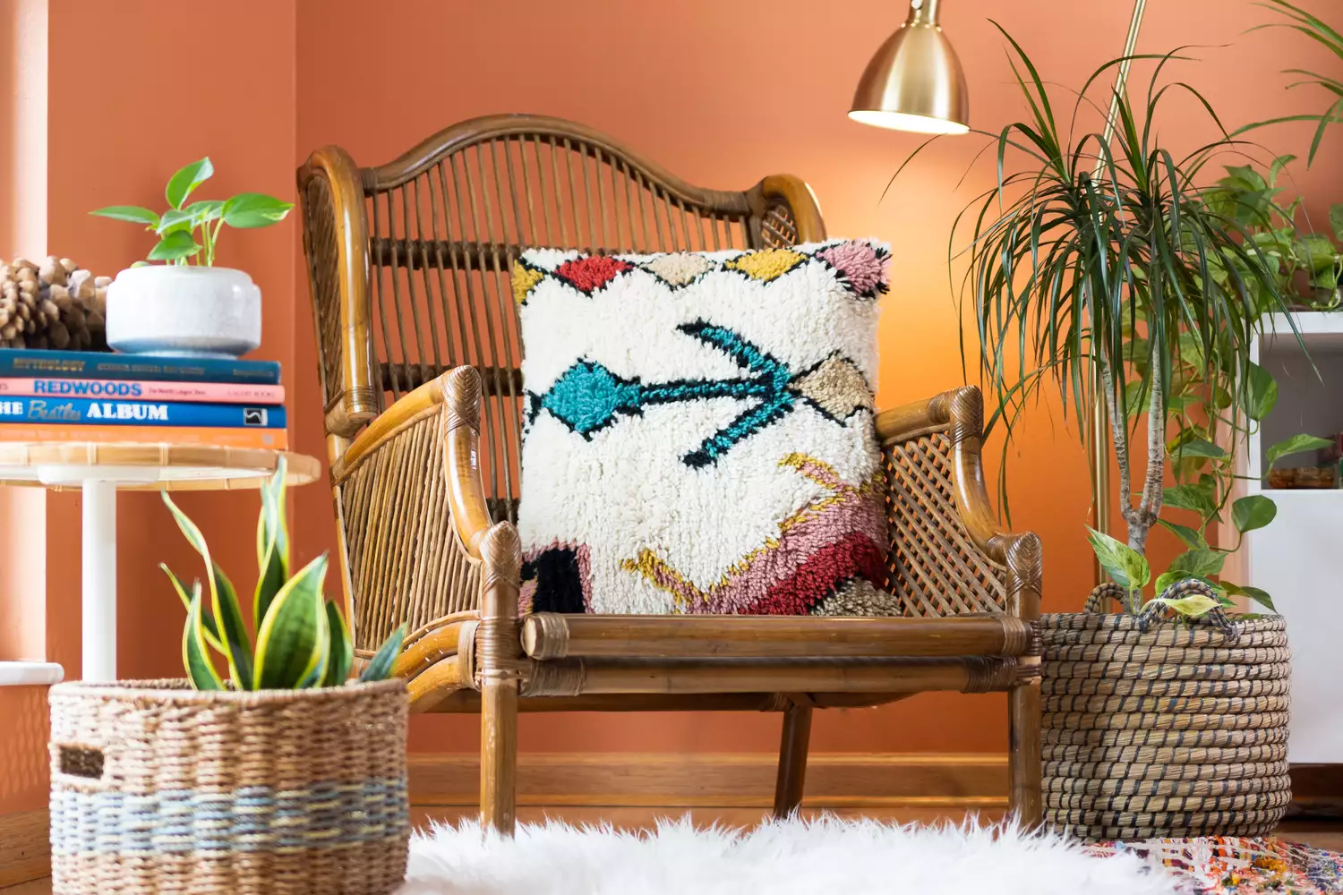 Rattan chair with colorful throw pillow on top and surrounded with houseplants