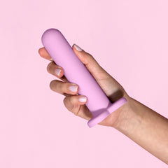 Light pink background with a hand with white nail polish holding light pink anal dilator