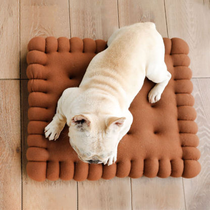 A brown biscuit shaped dog cushion bed on the floor, and a Pug lying on it.