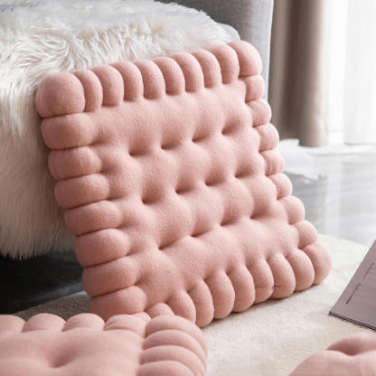 A pink biscuit shaped dog cushion bed standing next to the sofa.