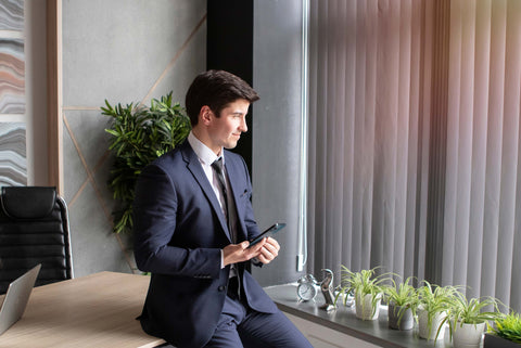 Attractive man in two-piece suit sitting wooden table in office with flower decorations